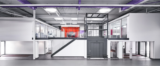 Blick aus der Produktionshalle von ›Grohe Technology‹ in die verglaste Verwaltungsebene mit Treppenanlage und Besprechungsraum als transparente Verbindung zwischen Fertigung und Bürobereichen, geplant und realisiert von arcplus Architekten