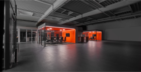 Produktionshalle von ›Grohe Technology‹ mit bewusst integrierten, verglasten Besprechungsboxen als Teil eines New-Work-Konzepts, das Kommunikation, Transparenz und kurze Wege direkt in der industriellen Arbeitsumgebung ermöglicht, geplant und realisiert von arcplus Architekten