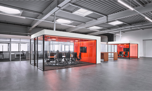 Verwaltungsbereich von ›Grohe Technology‹ mit freistehenden, verglasten Raum-in-Raum-Systemen und akustisch wirksamen Innenflächen als integrierte Besprechungsräume innerhalb der Industriearchitektur, geplant und realisiert von arc+ Architekten