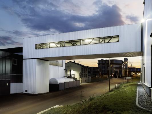 Stählerne Verbindungsbrücke im Projekt Oest, die Produktions- und Versandgebäude funktional und konstruktiv über die öffentliche Erschließung hinweg verbindet – entworfen von arc+