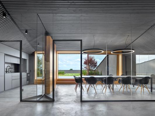 Innenansicht des Bürogebäudes ›Büro am Stadtbahnhof‹ mit gläsern abgetrenntem Besprechungsbereich, integrierter Küche, sorgfältig abgestimmter Möblierung und zurückhaltender Lichtgestaltung, geplant und realisiert von arcplus Architekten